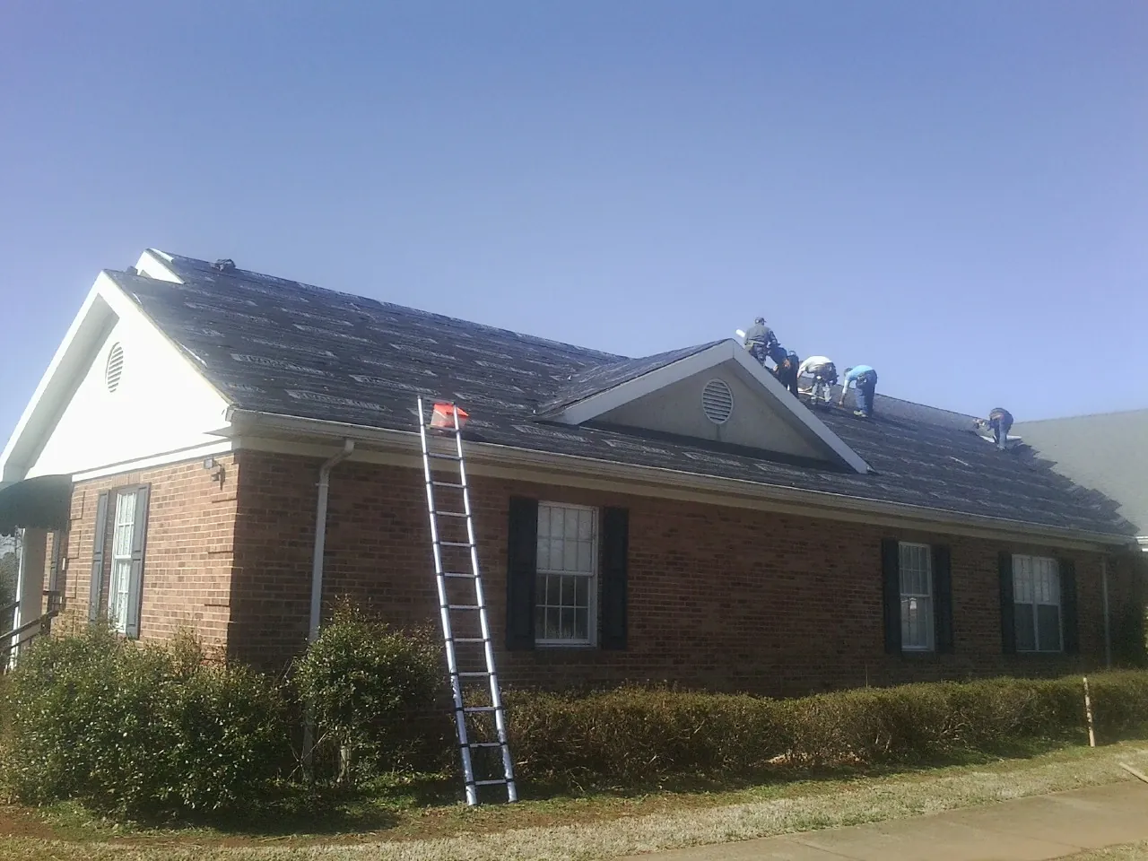 Crew tearing shingles off a brick ranch roof with a ladder set — Emergency Roof Repair work by our crew in Sparland
