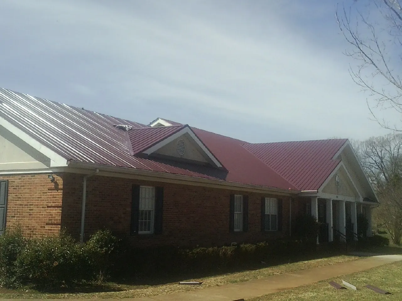 Red metal roof with gabled entries on a long brick building, from a Hail Damage Roof Repair job in Sparland