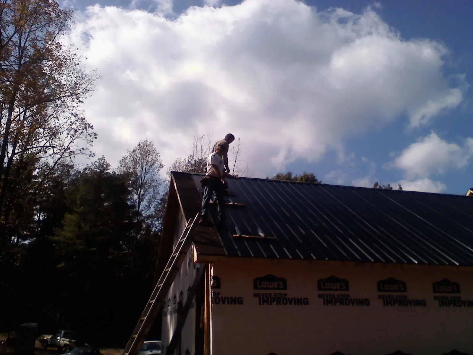 Roofer fastening dark metal panels high against a cloudy sky, from a Roof Inspection job in Sparland