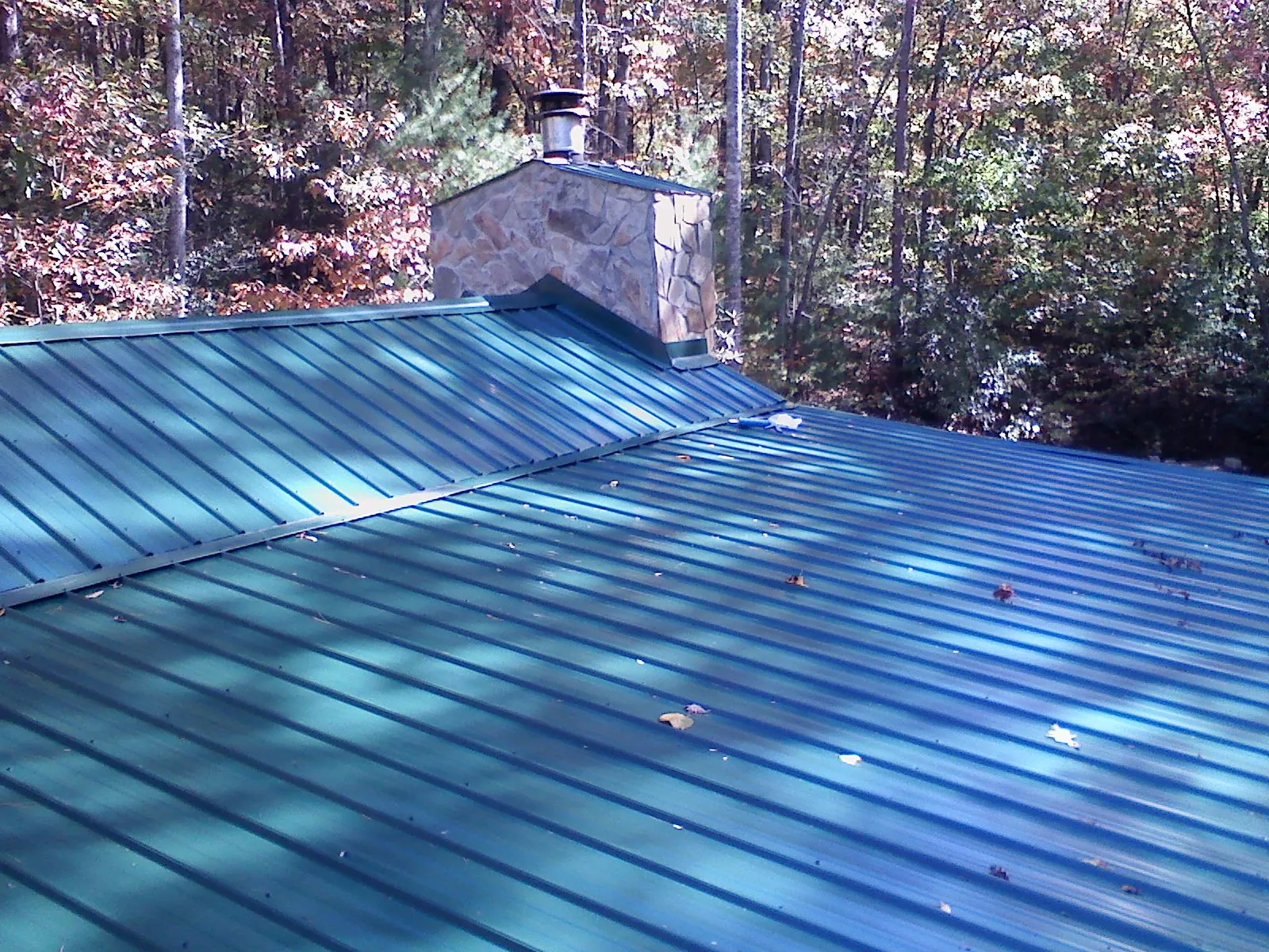 New green metal roof and stone chimney surrounded by autumn woods in Sparland