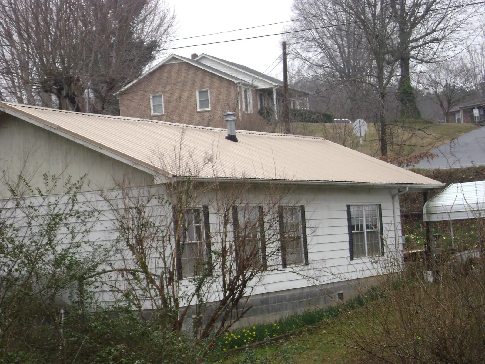 Tan metal roof on a white sided house set into a hillside — Commercial Roofing by Roofing Brothers in Sparland